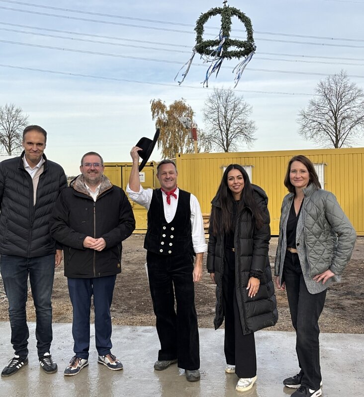 Fünf Personen vor einem gelben Baucontainer, oben eine Richtkrone
