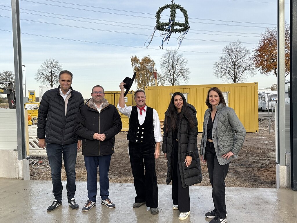 Fünf Personen vor einem gelben Baucontainer, oben eine Richtkrone