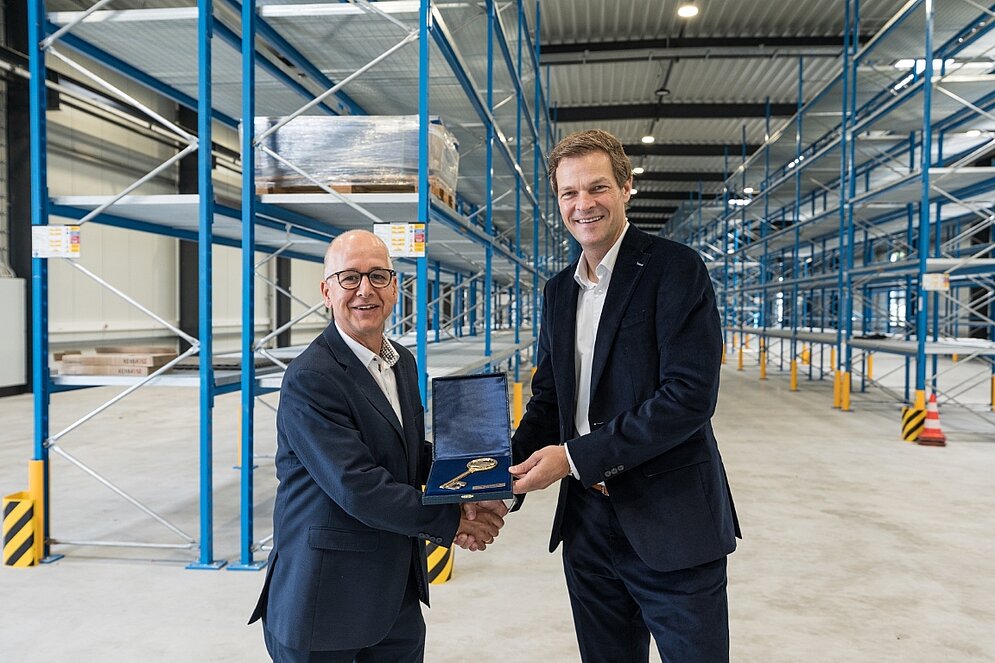 Zwei Personen in einer Lagerhalle mit einem goldenen Schlüssel in der Hand