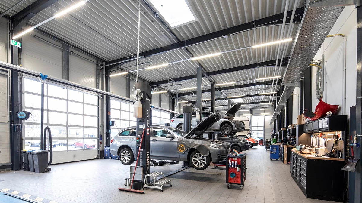 Innenansicht einer großen, sauberen Kfz-Werkstatt mit Hebebühnen und einem Auto auf einer Bühne