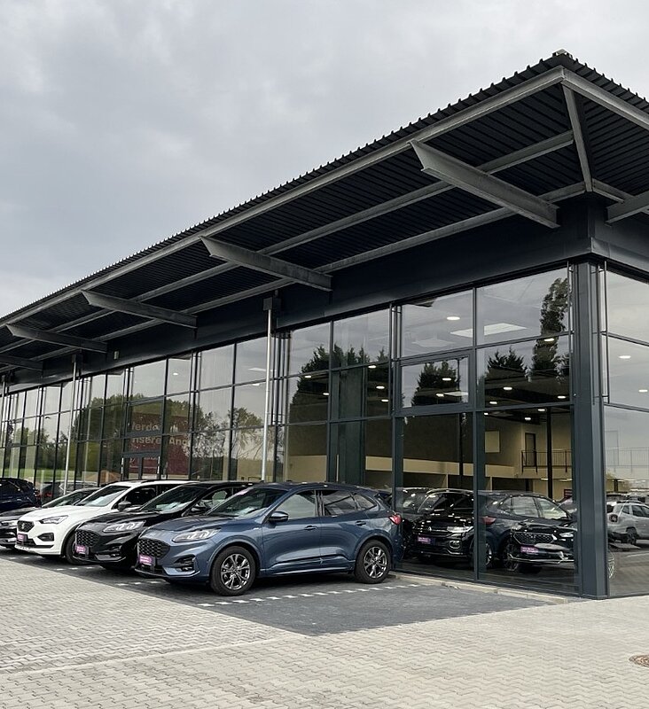 Modernes AGVV Autohaus mit Glasfront und gepflastertem Vorplatz, auf dem mehrere Neuwagen stehen