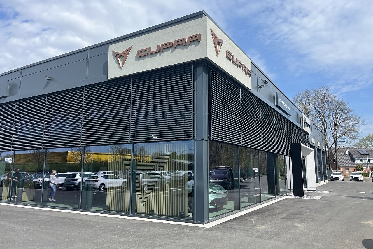 Eckansicht des modernen Cupra Autohauses mit großflächiger Glasfassade und Logo