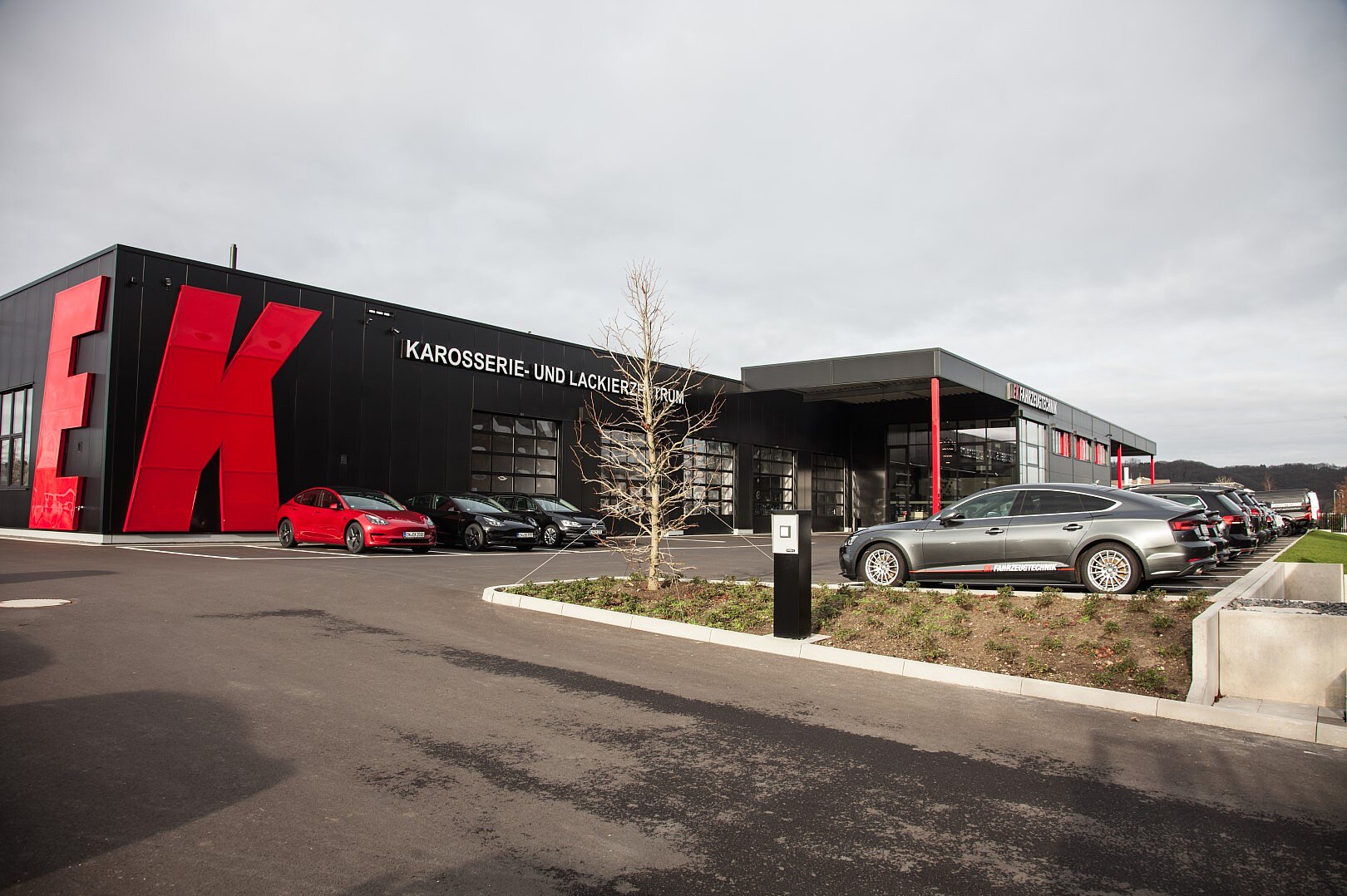 Außenansicht eines modernen Karosserie- & Lackierbetriebs mit schwarzer Fassade und großem rotem Firmenlogo