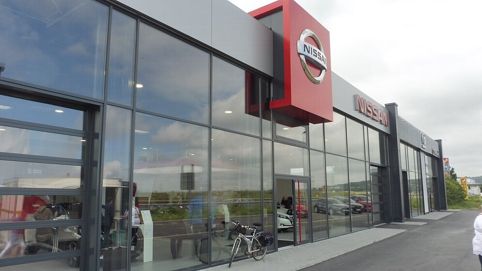 Seitenansicht des modernen Nissan Autohauses mit großer Glasfront und grauer Fassade