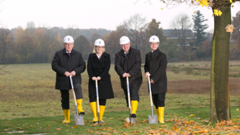 4 Mitarbeitende mit Spaten und Gummistiefeln auf einem Grundstück