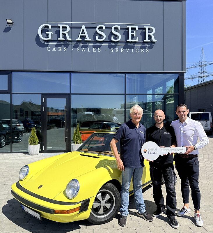 drei Personen mit Schlüssel in der Hand vor gelbem Porsche