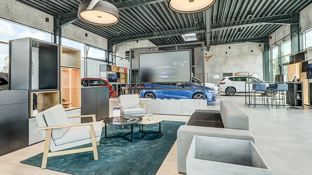 vGemütliche Kundenlounge im Ausstellungsraum mit modernen Möbeln und Industrie-Decke