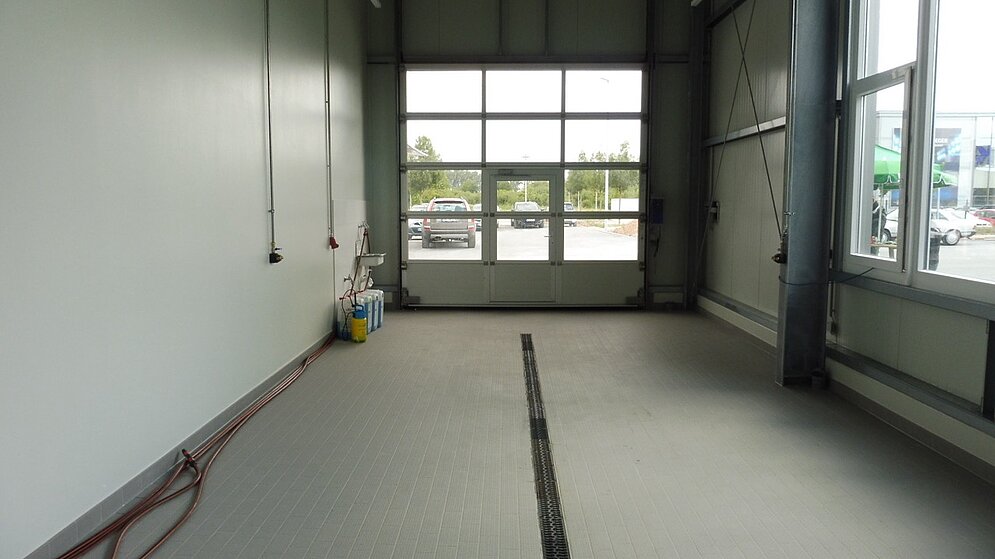 Leerer Fahrzeugübergaberaum oder Direktannahme mit grauem Fliesenboden und Sektionaltor