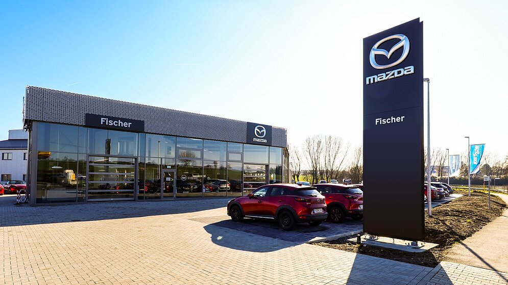 Außenansicht des schlüsselfertigen Mazda Autohaus Fischer mit Werbepylon und Glasfassade