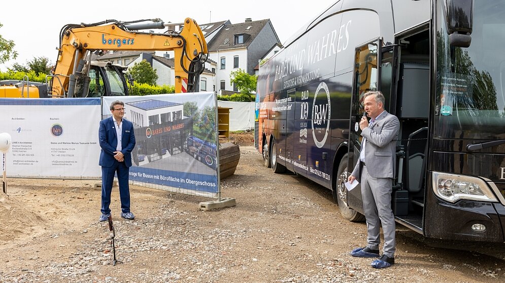 Zwei Personen mit Bus und Bagger im Hintergrund