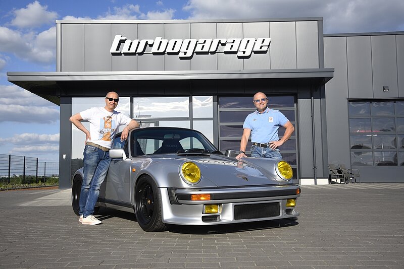 zwei Männer mit einem Porsche vor einer Werkstatt 