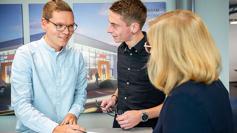 Drei Personen, zwei Männer und eine Frau, besprechen Baupläne an einem Tisch