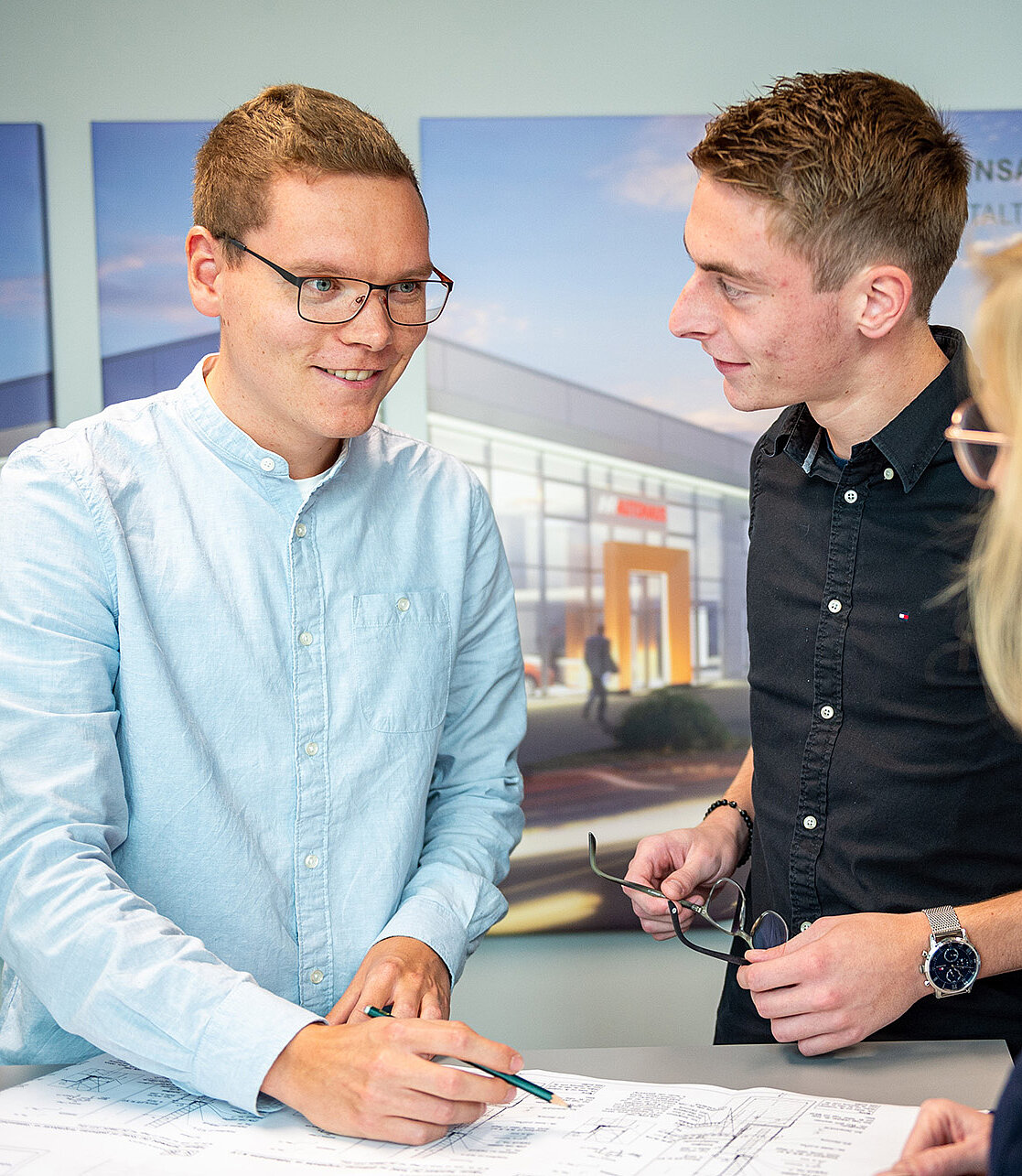 Drei Personen, zwei Männer und eine Frau, besprechen Baupläne an einem Tisch