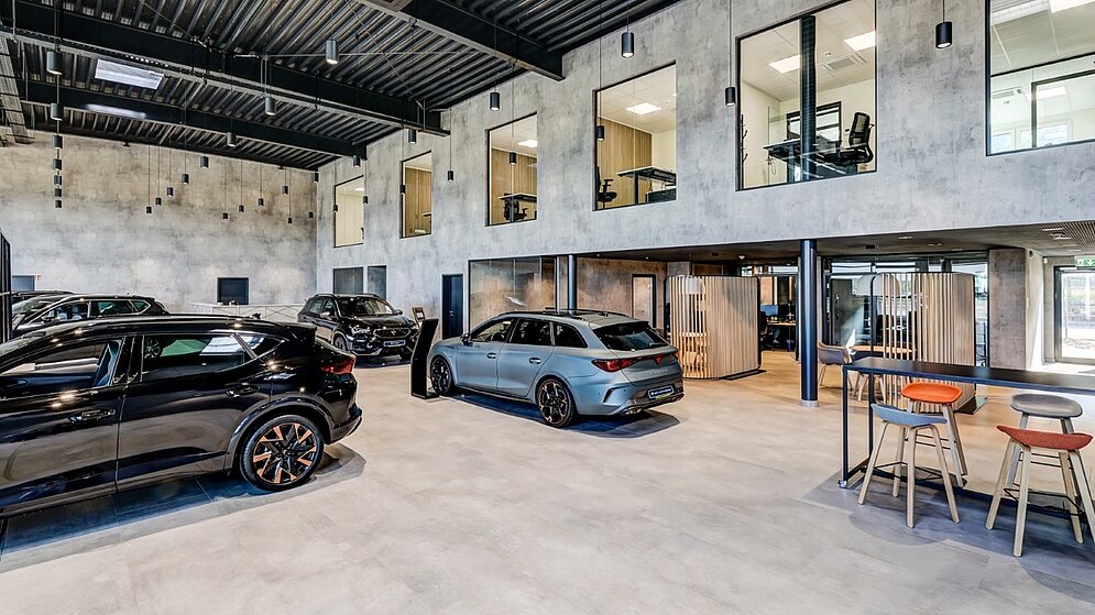 Innenansicht einer großen Autohalle mit ausgestellten Fahrzeugen und modernem Loungebereich