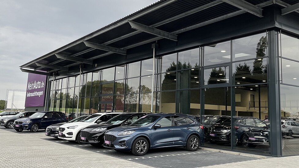 Moderne Glasfront des AGVV-Autohauses mit ausgestellten Fahrzeugen davor.