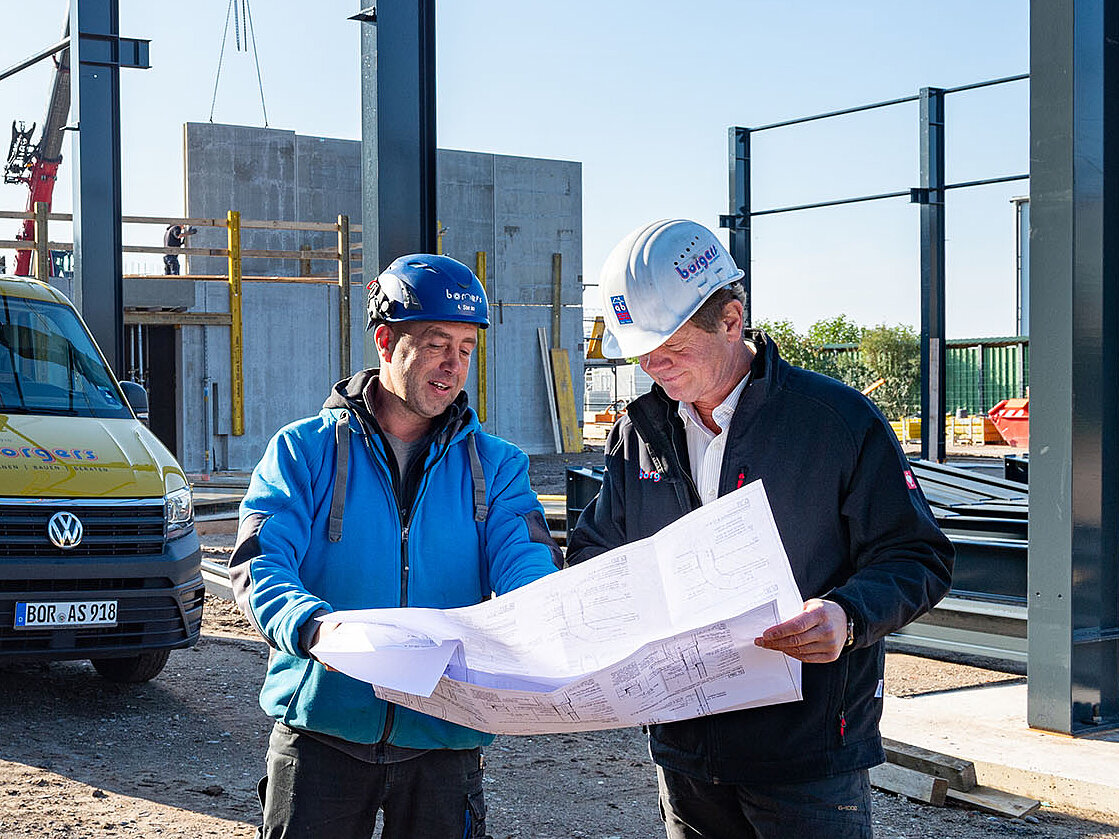 Zwei Mitarbeiter blicken auf der Baustelle auf einen Plan