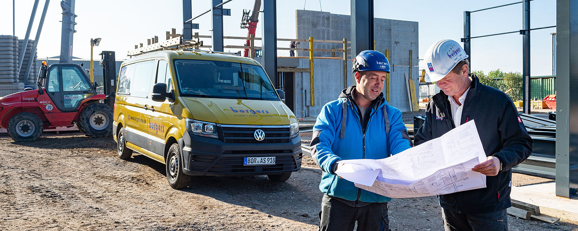 Zwei Mitarbeiter blicken auf der Baustelle auf einen Plan