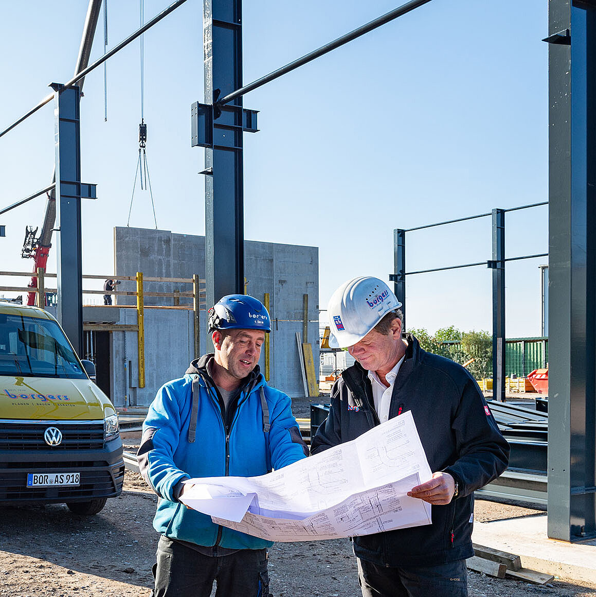 Zwei Mitarbeiter blicken auf der Baustelle auf einen Plan