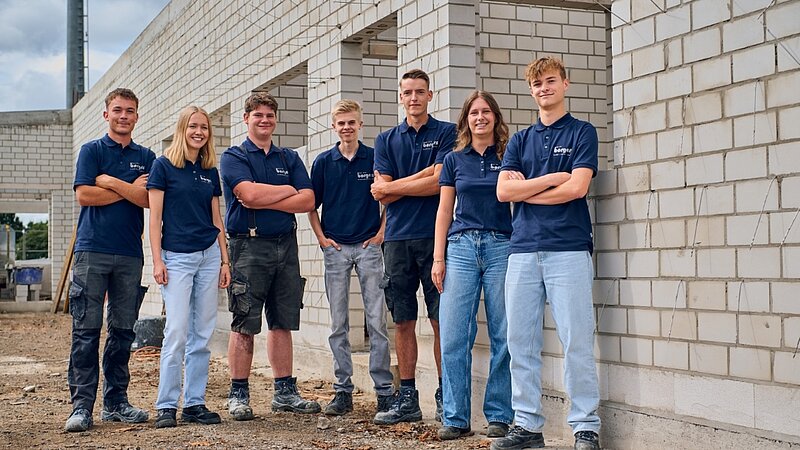 Gruppe junger Auszubildender mit dunkelblauen Shirts auf der Baustelle