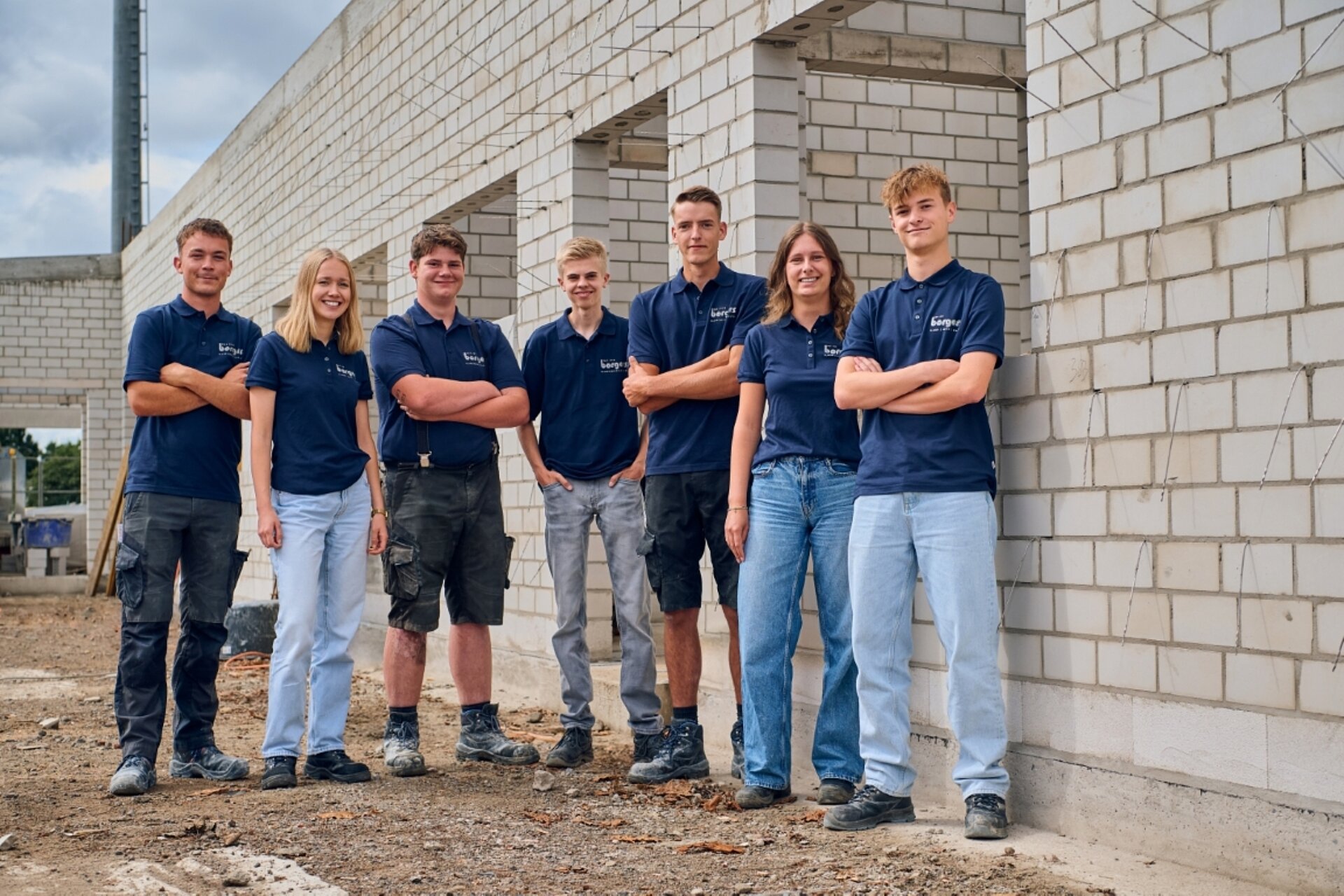 Gruppe junger Auszubildender mit dunkelblauen Shirts auf der Baustelle