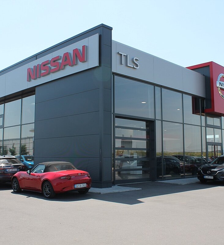 Außenansicht des schlüsselfertigen Autohaus Gerding mit Nissan-Branding und Fahrzeugen