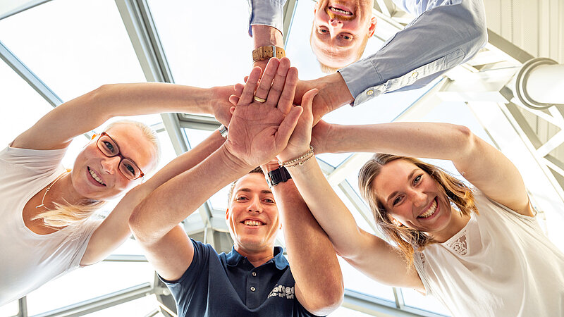 Vier Mitarbeitende stehen im Kreis und legen die Hände übereinander