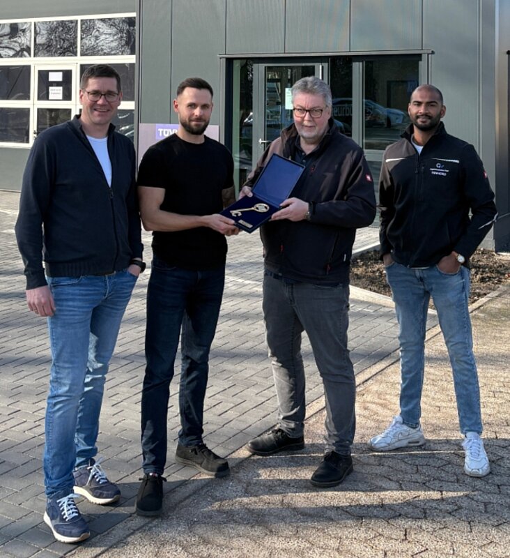 vier Personen vor einem Gebäude mit einem goldenen Schlüssel in der Hand