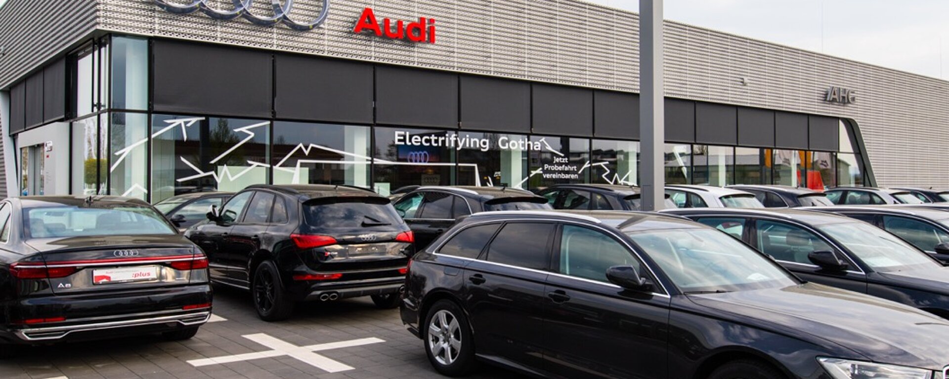 Außenansicht eines modernen Autohauses mit Verkaufsbereich und vielen E-Autos auf dem Gelände