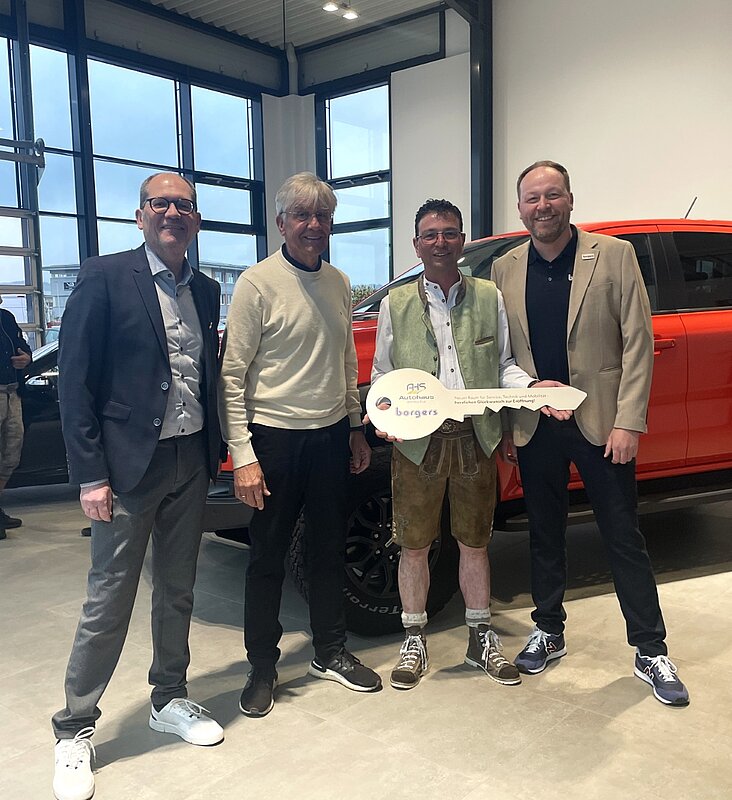 vier Männer mit einem Schlüssel in der Hand, rotes Auto im Hintergrund