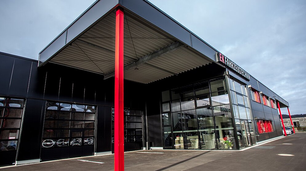 Frontansicht eines modernen Autohauses in Schwarz mit großer Glasfassade und roter Säule