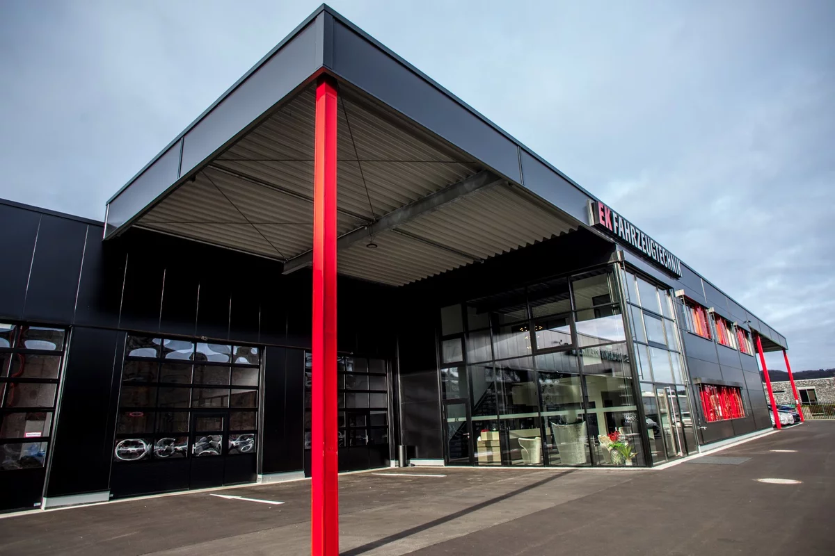 Frontansicht eines modernen Autohauses in Schwarz mit großer Glasfassade und roter Säule