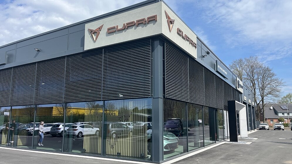 Eckansicht des modernen Cupra Autohauses mit großflächiger Glasfassade und Logo