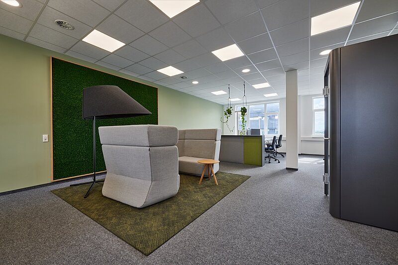 Lounge- und Empfangsbereich in einem modernen Bürogebäude mit einem großen vertikalen Pflanzenelement. 