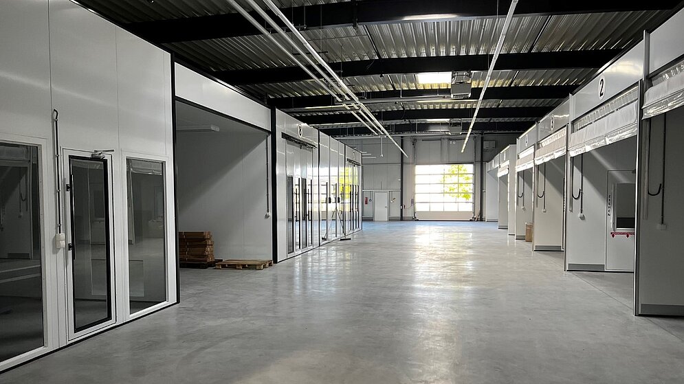 Innenansicht einer großen, leeren Werkstatthalle mit Sektionaltoren und Betonboden