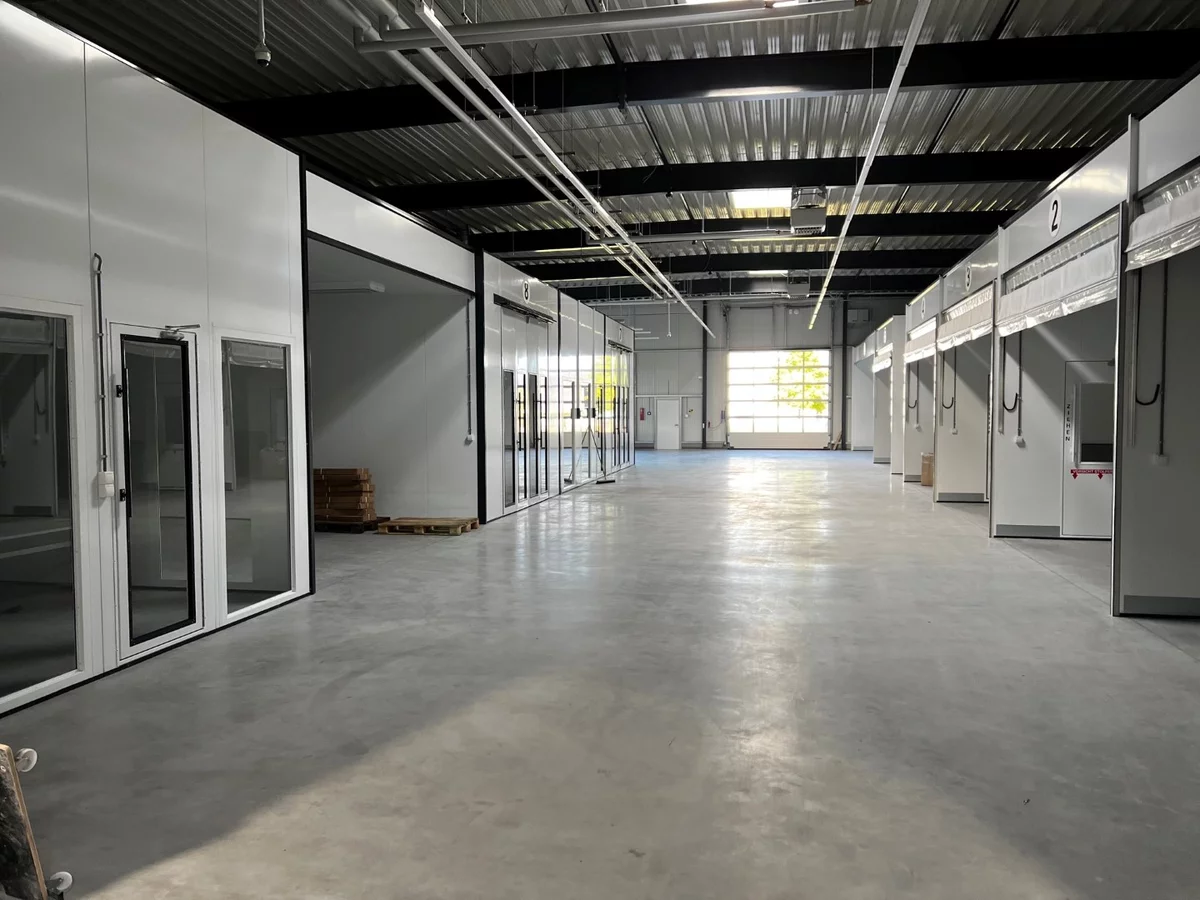 Innenansicht einer großen, leeren Werkstatthalle mit Sektionaltoren und Betonboden