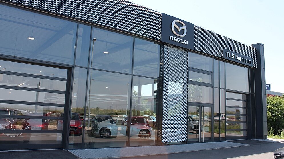 Detail der gläsernen Eingangsfassade mit Mazda-Logo und moderner Gebäudestruktur