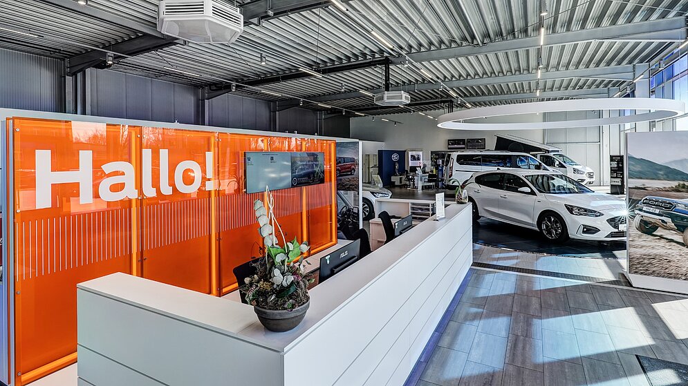 Empfangsbereich im Autohaus mit oranger Hallo-Wand und moderner Innenausstattung