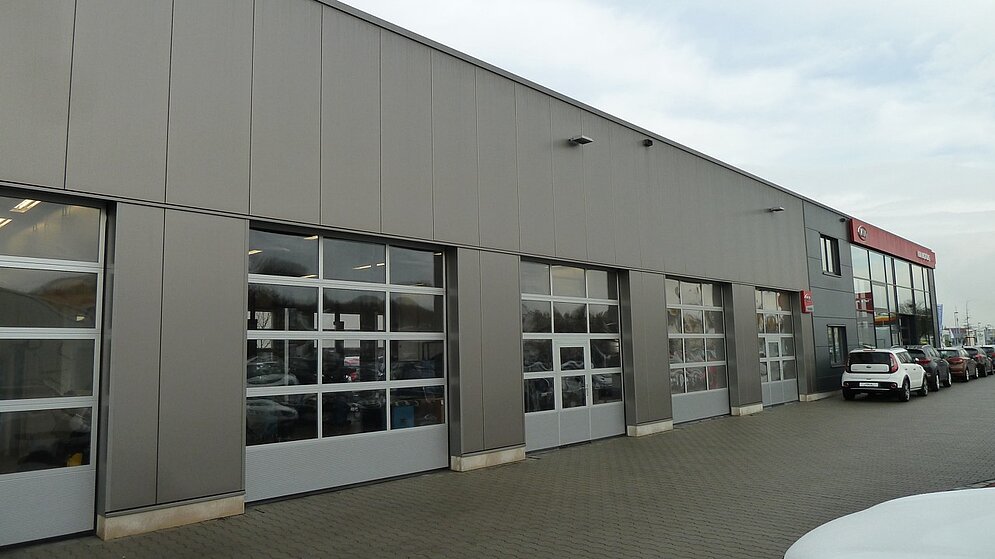 Außenansicht des Werkstattbereichs mit grauer Fassade und verglasten Sektionaltoren