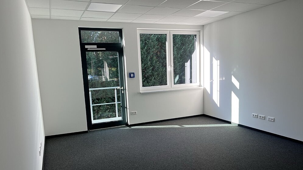 Leeres, unmöbliertes Büro mit dunklem Teppichboden und Fensterfront