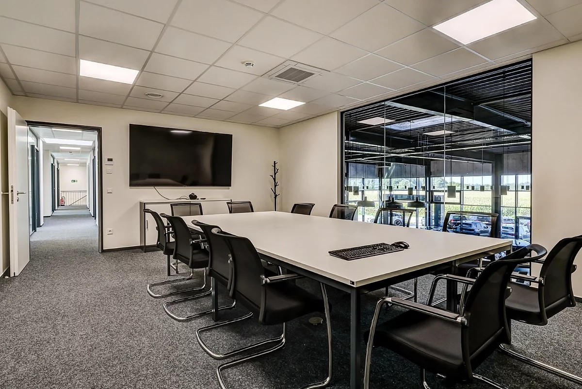  Besprechungsraum in einem Bürogebäude mit großem Konferenztisch, Stühlen und einem Fernseher an der Wand