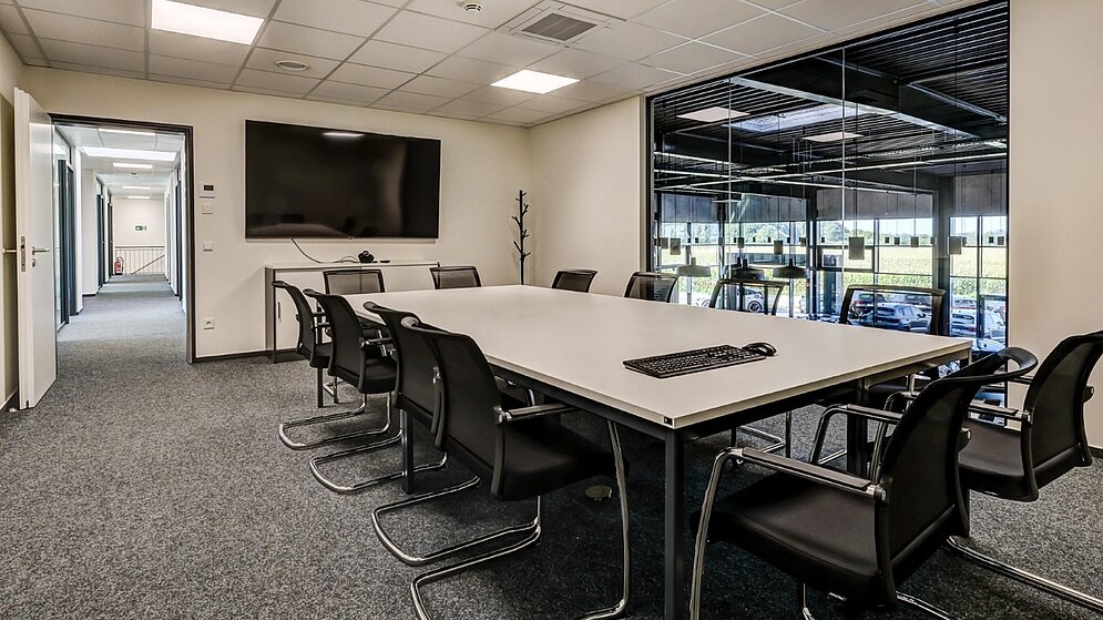 Besprechungsraum in einem Bürogebäude mit großem Konferenztisch, Stühlen und einem Fernseher an der Wand