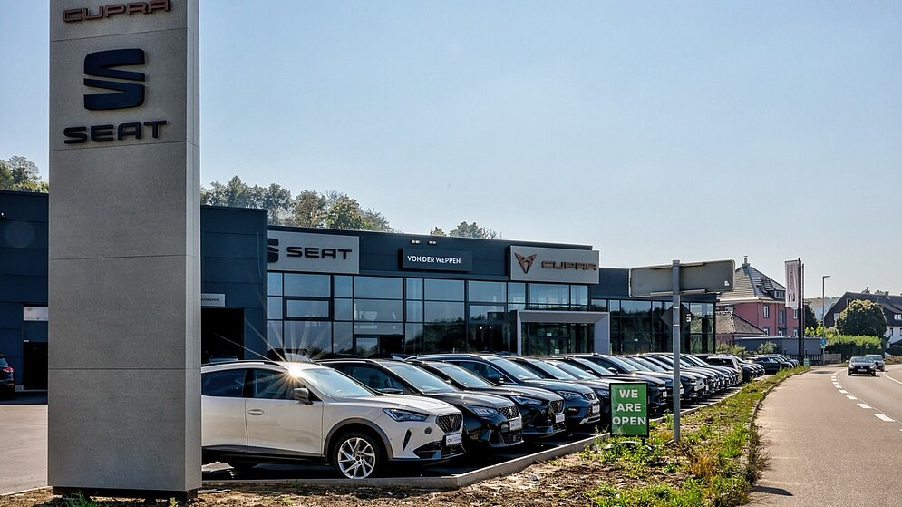 Außenansicht eines modernen Autohauses mit Verkaufsbereich und vielen Neuwagen auf dem Gelände