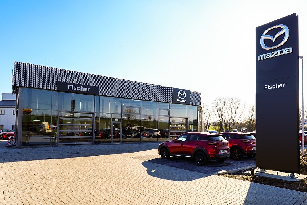 Außenansicht des schlüsselfertigen Mazda Autohaus Fischer mit Werbepylon und Glasfassade