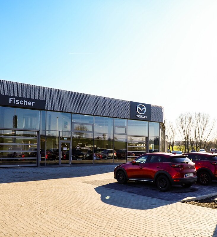 Außenansicht des schlüsselfertigen Mazda Autohaus Fischer mit Werbepylon und Glasfassade
