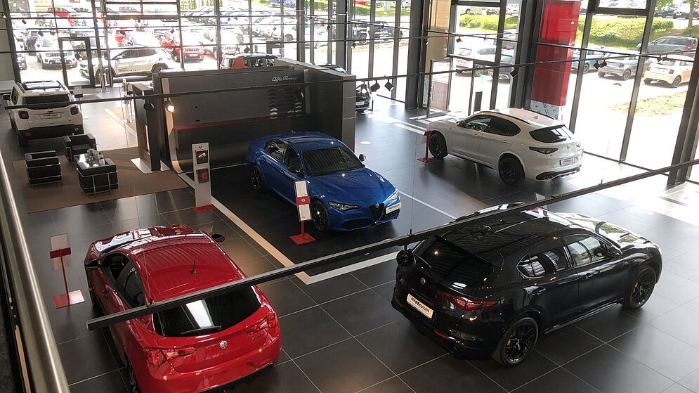 Blick in den hellen Verkaufsraum des Autohauses mit Fahrzeugausstellung und Fliesenboden