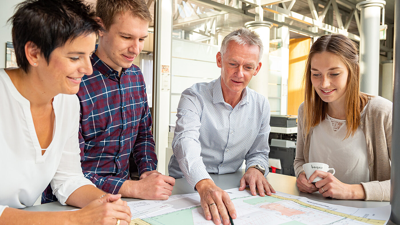 4 Mitarbeitende blicken auf einen Bauplan