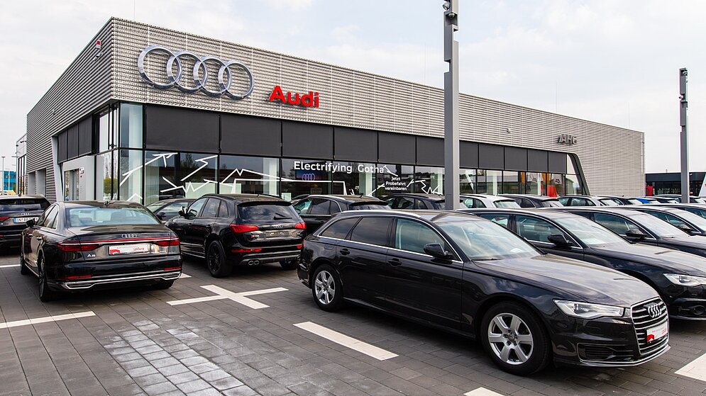 Außenansicht eines modernen Autohauses mit Verkaufsbereich und vielen E-Autos auf dem Gelände