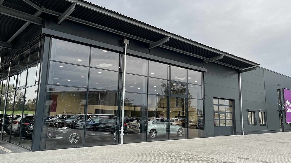 Großflächige Glasfront des AGVV-Autohauses, in dem Autos ausgestellt sind, frontal aufgenommen. 