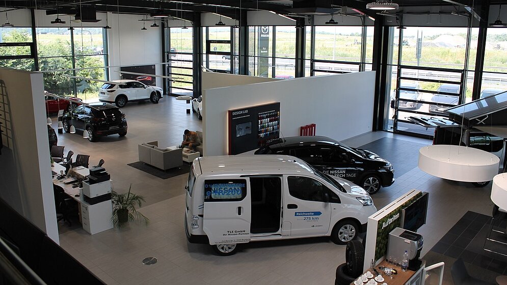 Überblick über den lichtdurchfluteten Showroom mit Fahrzeugpräsentation von der Galerie