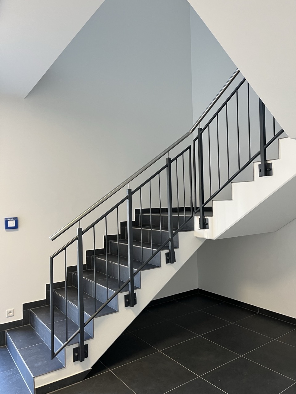 AGVV-Treppenhaus mit grauem Teppichboden und schwarzen Metallgeländern in einem Verwaltungsgebäude.